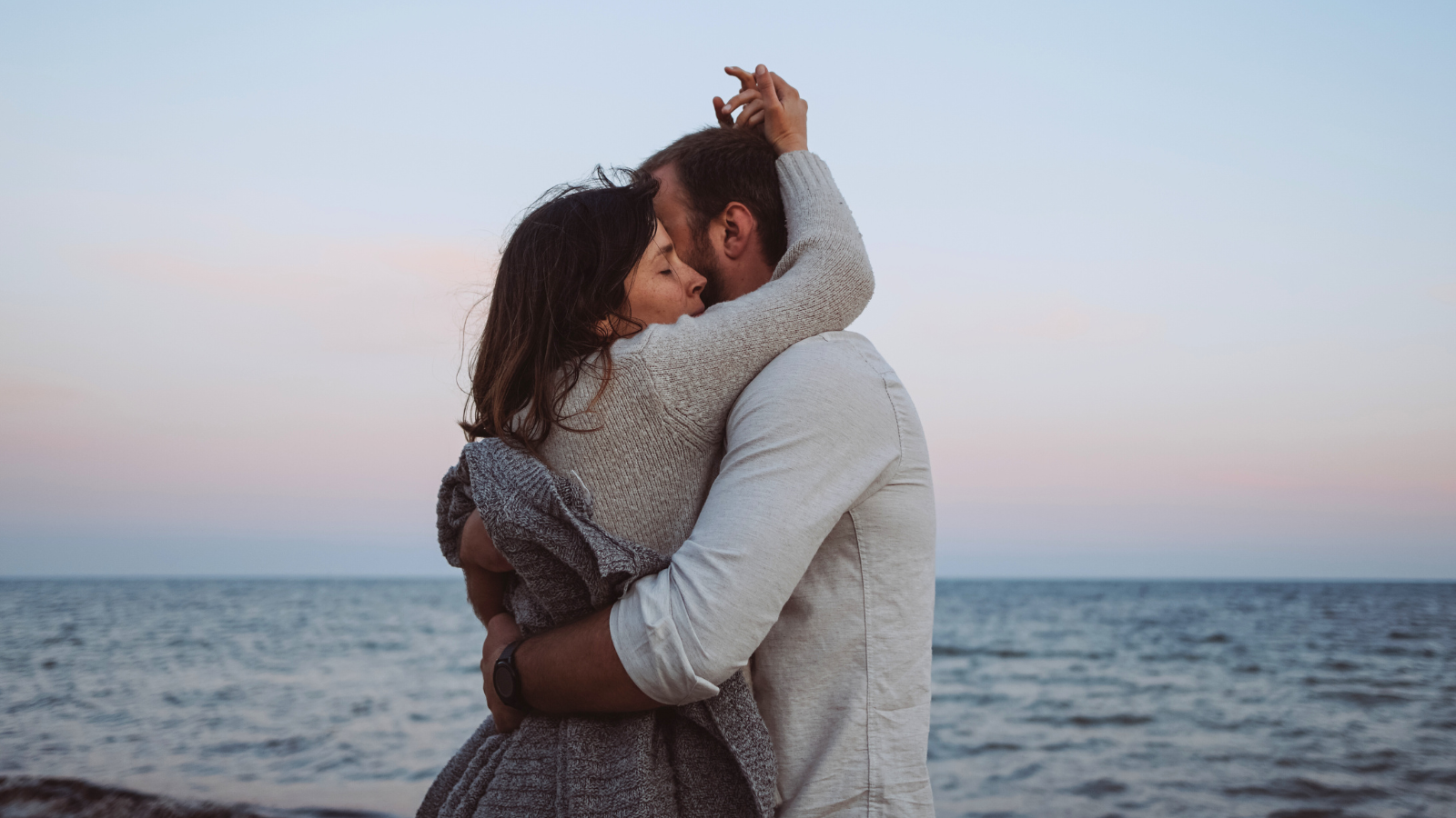 Un couple s’enlace tendrement face à la mer, dans une lumière douce de fin de journée — une scène empreinte d’émotion, parfaite pour illustrer la puissance des tropes romantiques.