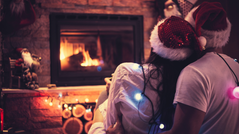 Couple enlacé devant une cheminée allumée, dans une ambiance chaleureuse et romantique de Noël.